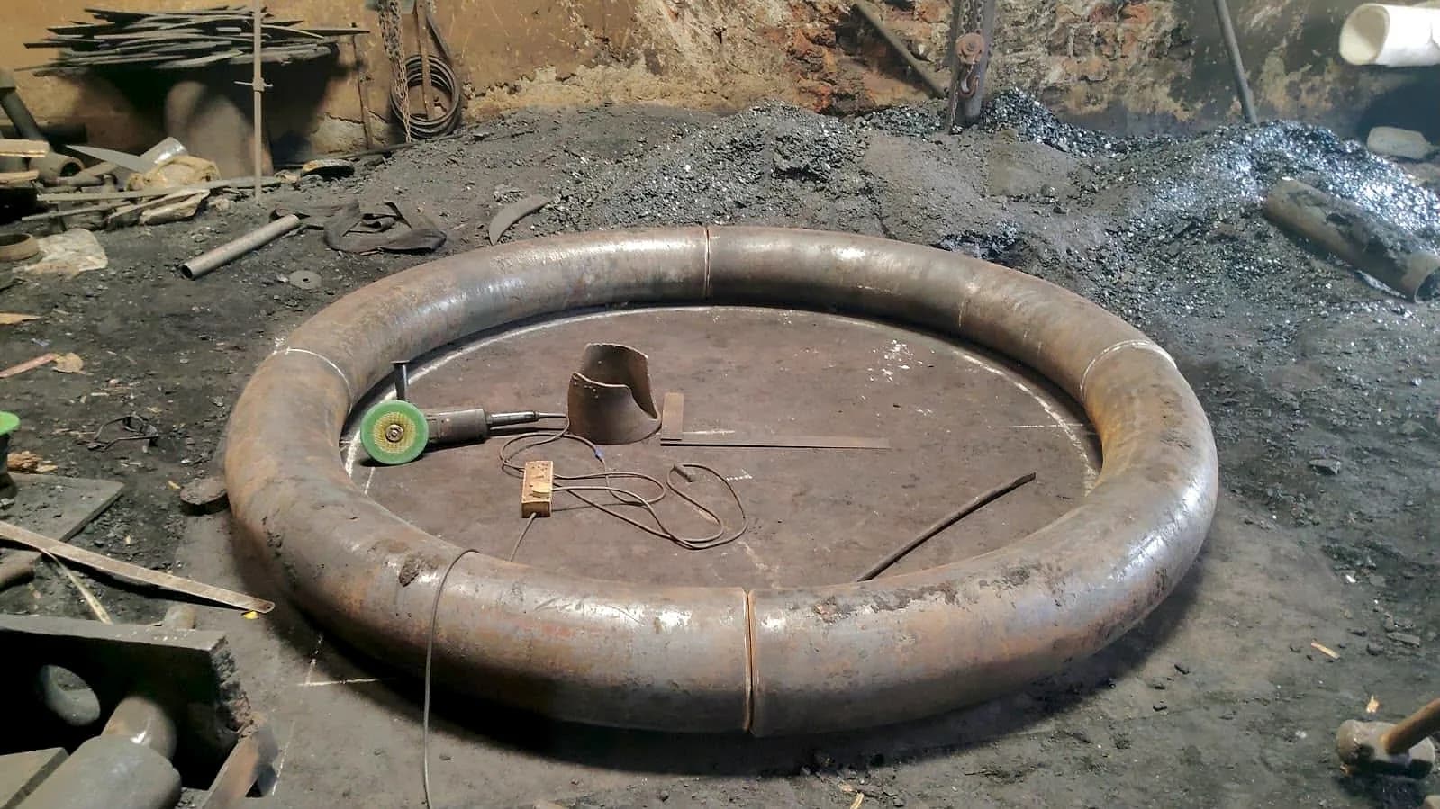 A carbon steel pipe bent into a complete 360 degree ring, lying on the works floor