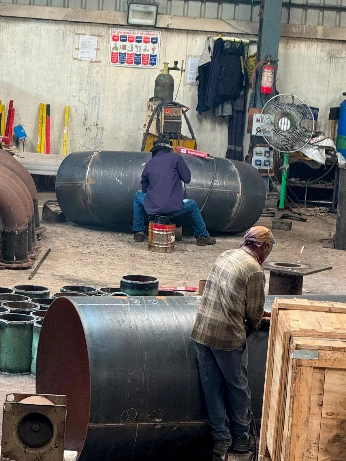 Fabricators working on large diameter pipe sections in the fabrication bay