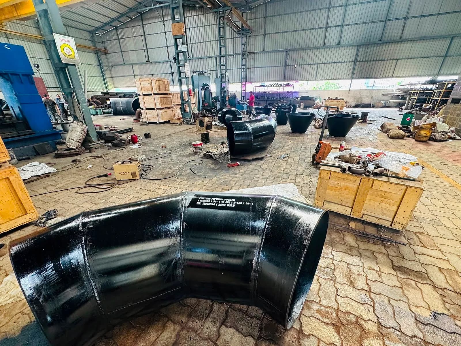 A finished black mitre bend in the foreground of the works floor, crates and fittings behind