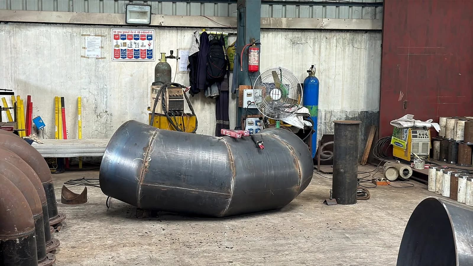 A large diameter mitre elbow lying in the fabrication bay among welding equipment