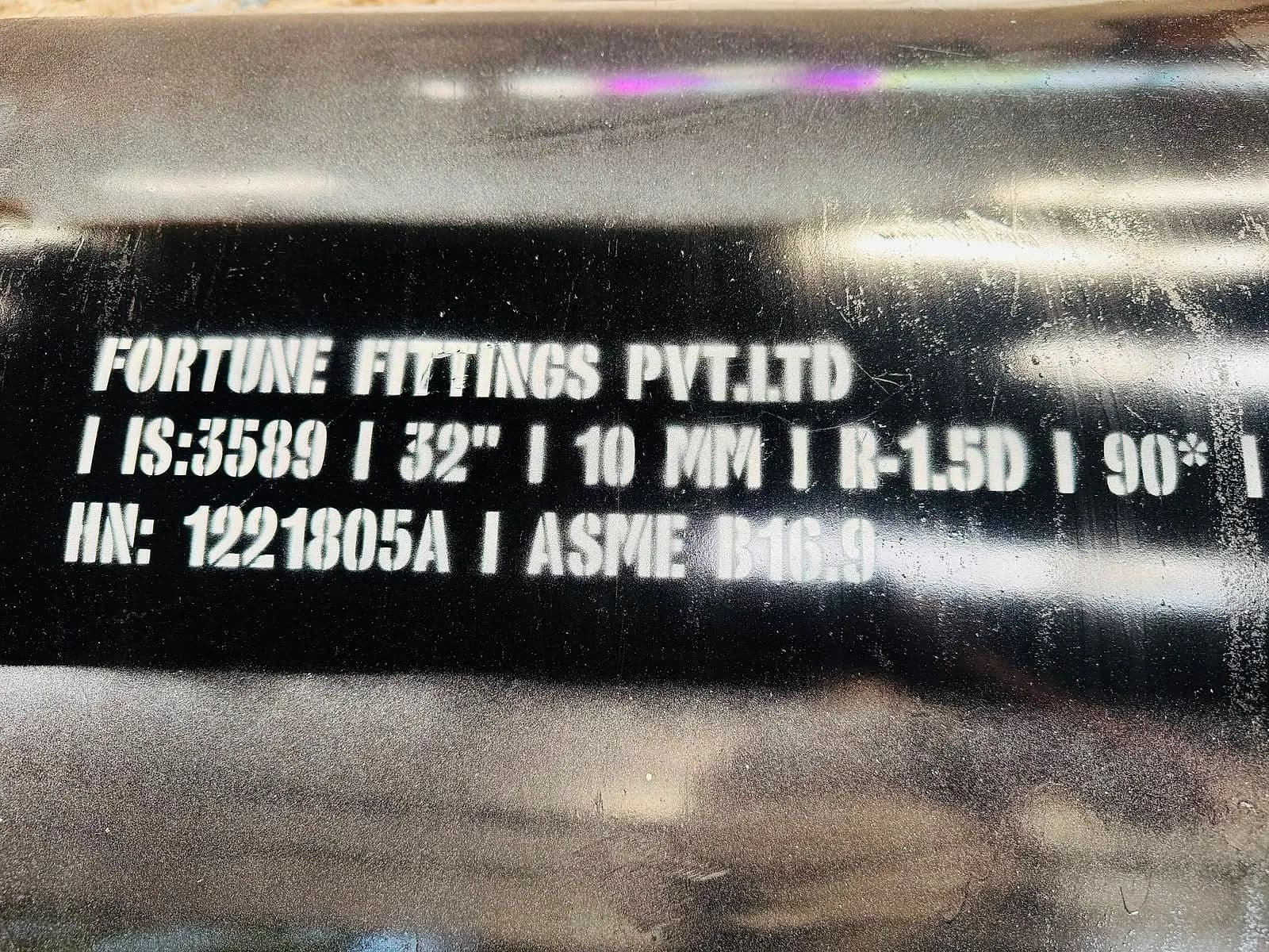 White stencilled marking on a black fitting reading Fortune Fittings Pvt Ltd, IS 3589, 32 inch, 10 mm, R-1.5D, 90 degrees, ASME B16.9