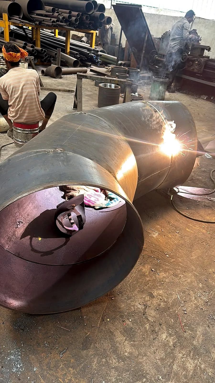 A welder working on the joint between two segments of a large mitre bend, sparks visible