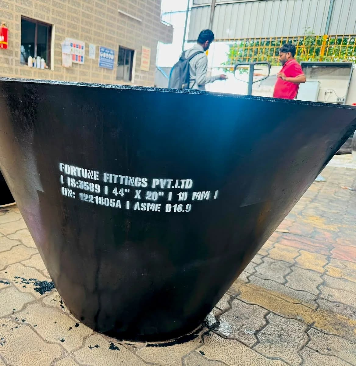 A large black fabricated concentric reducer standing on its small end, with stencilled marking